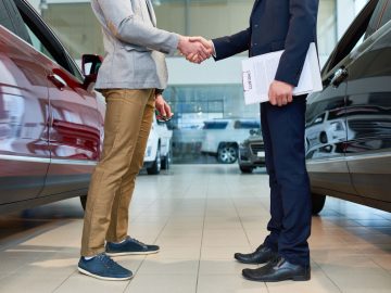 Twee mannen schudden elkaar de hand in een autoverkoopshowroom.