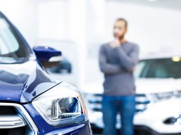 Een man kijkt naar een blauwe auto in een showroom en overweegt de verzekeringspremie.