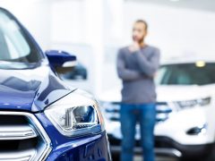 Een man kijkt naar een blauwe auto in een showroom en overweegt de verzekeringspremie.