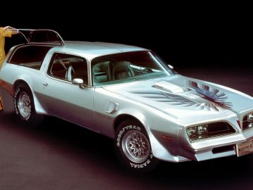 Een vrouw die naast een zilveren kammback Pontiac Firebird staat.