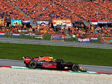 Een rode Formule 1-raceauto op een circuit in Zandvoort voor een publiek.