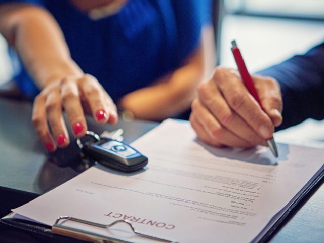 Een persoon die een autoverkoopcontract ondertekent met een pen en een autosleutel.