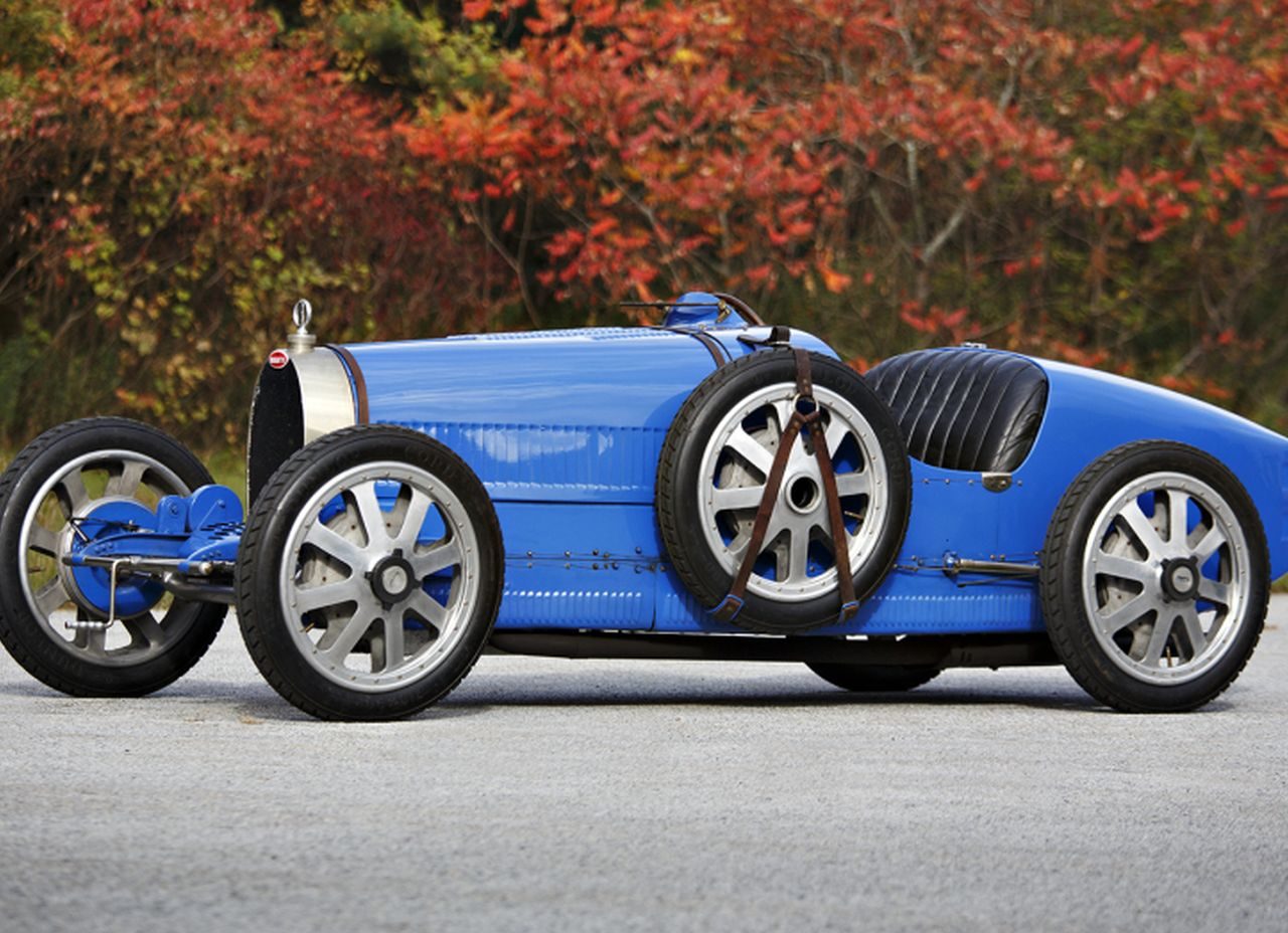 Een blauwe vintage Bugatti-raceauto staat geparkeerd op een weg.