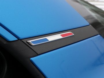 Een blauwe Alpine A110 met een rood, wit en blauw embleem.
