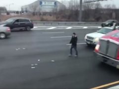Een man staat naast een semi-vrachtwagen op de Amerikaanse snelweg waar geld ligt voor het oprapen.