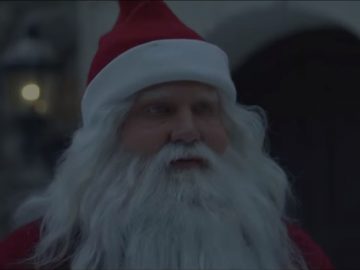 Een man verkleed als Kerstman staat voor een gebouw.