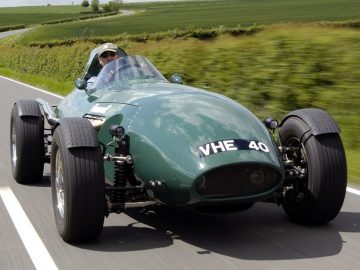 Een groene Vanwall-raceauto die over een landweg rijdt.