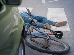 Een persoon die met een fiets voor een auto op de grond ligt, wat het belang van verkeersveiligheid benadrukt.