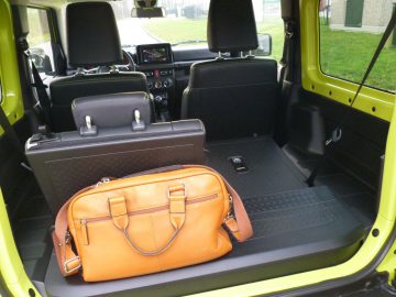 Een gele Suzuki Jimny met een bruine tas op de achterbank.