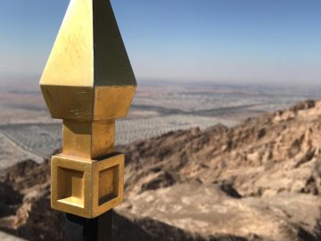 Een gouden puntig voorwerp op een zwarte paal met op de achtergrond het Jebel Hafeet-landschap.