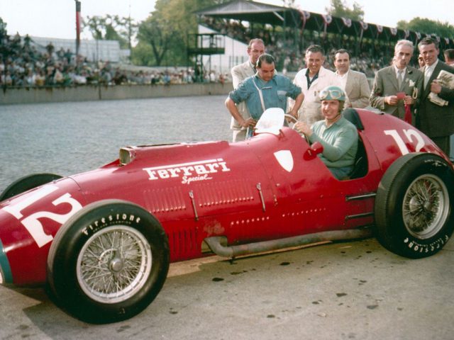 Een man staat naast een rode Indy-racewagen.