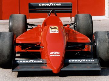 Een rode Ferrari Indy-raceauto geparkeerd voor een rode garage.