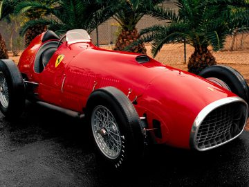 Een Indy-rode Ferrari-raceauto staat geparkeerd voor palmbomen.