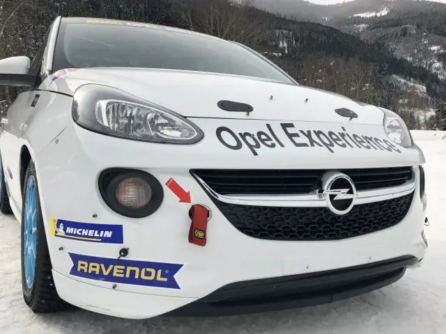 Een witte Adam R2-auto met het woord Opel erop staat geparkeerd in de sneeuw.
