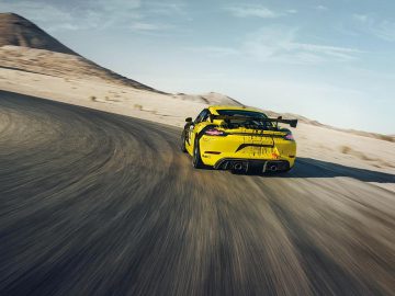 Een gele Porsche Cayman-sportwagen rijdt over een woestijnweg.