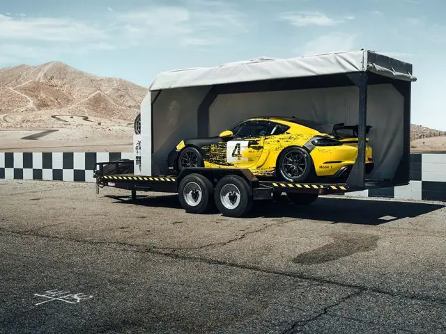 Een gele Porsche Cayman-auto zit achterin een aanhangwagen.