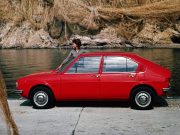 Een vrouw die naast een rode Alfa Romeo staat.