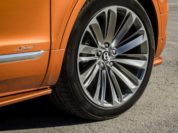 Een close-up van de wielen van een oranje Bentley Bentayga Speed SUV.
