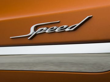 Een close-up van de snelheidsbadge op een oranje Bentley Bentayga Speed.