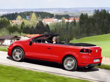 Een rode Volkswagen Golf Cabriolet cabriolet rijdt over een landweg.