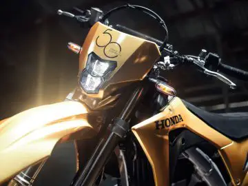 Een gouden Honda-crossmotor staat geparkeerd in een garage.