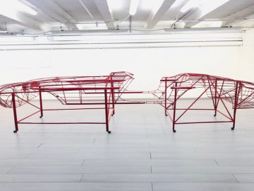 Twee Halmo rode metalen sculpturen in een lege ruimte.