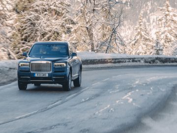 Een blauwe Rolls Royce Cullinan rijdt over een besneeuwde weg.