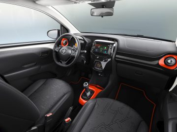 Het interieur van een Aygo-auto met oranje en zwarte accenten.