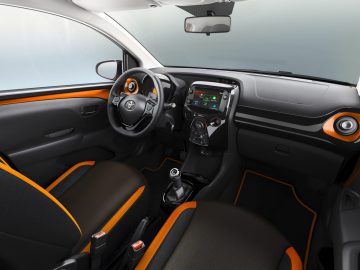 Het interieur van een Aygo-auto met oranje en zwarte accenten.