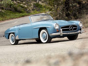 Een oude blauwe Mercedes-Benz SL roadster rijdt over de weg.