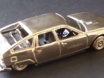 Een zilveren speelgoedauto van Tres Precieux Voitures op een zwarte ondergrond.