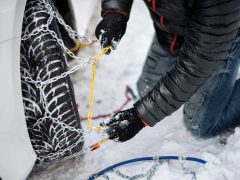 Een man legt kettingen op een auto voor een wintersportevenement in de sneeuw.
