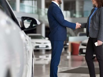 Een man en vrouw schudden elkaar de hand in een autoshowroom van BOVAG.
