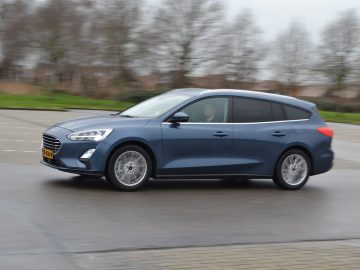 Een blauwe Focus rijdt op een natte weg.