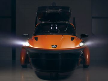 Een futuristische oranje Pal-V wordt getoond in een donkere kamer.
