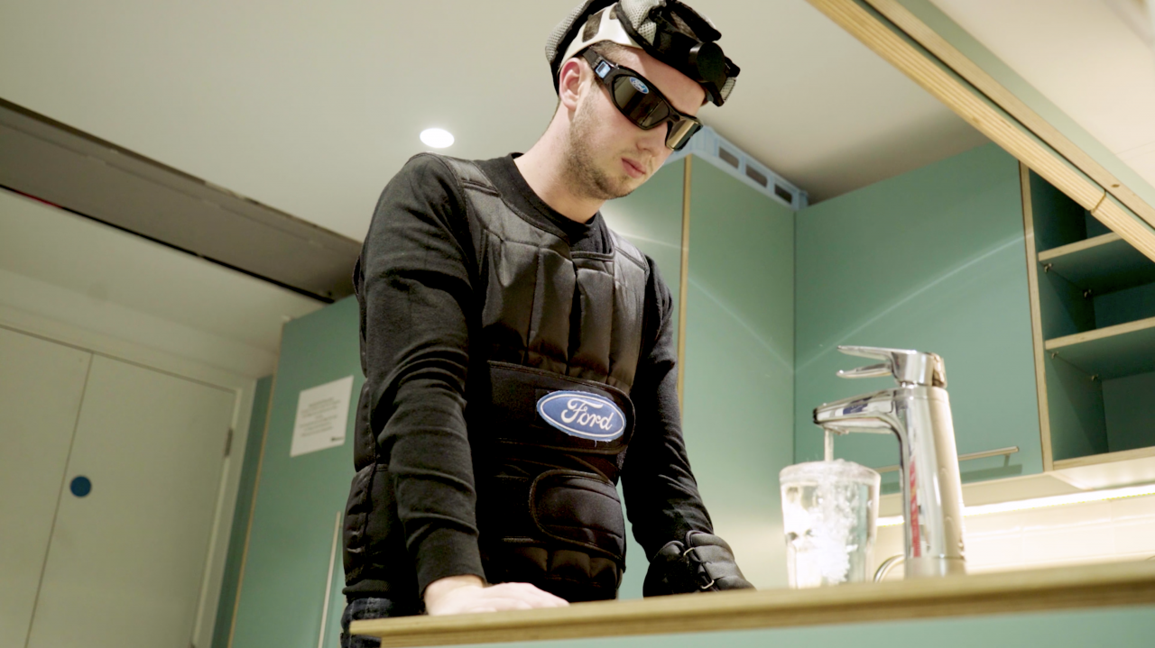 Een man in een beschermend pak, die tekenen van vermoeidheid vertoont, staat in een keuken.