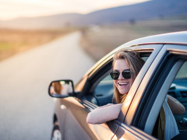 Een jonge vrouw rijdt met haar auto over een landweg, omringd door clichés van glooiende heuvels en gouden zonsondergangen.