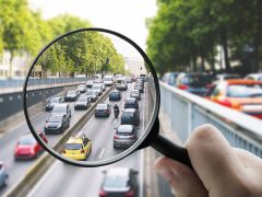 Een persoon houdt een vergrootglas boven een snelweg vol auto's en onderzoekt de impact op het klimaatplan.