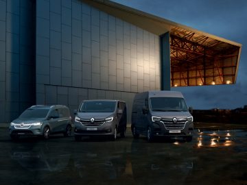 De nieuwe gefacelifte Renault Trafic-busjes staan 's nachts voor een gebouw geparkeerd.