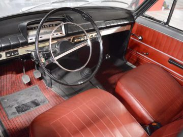 Het interieur van een klassieke auto met rood lederen stoelen en een 124 stuurwiel.