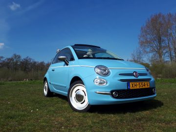 Een blauwe Fiat 500C Spiaggina '58 staat geparkeerd in een grasveld.