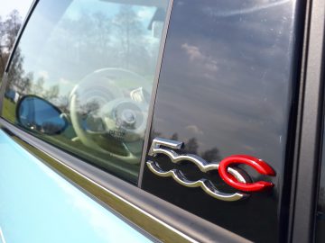 Een blauwe 500C Spiaggina '58 met een rood logo op de zijruit.