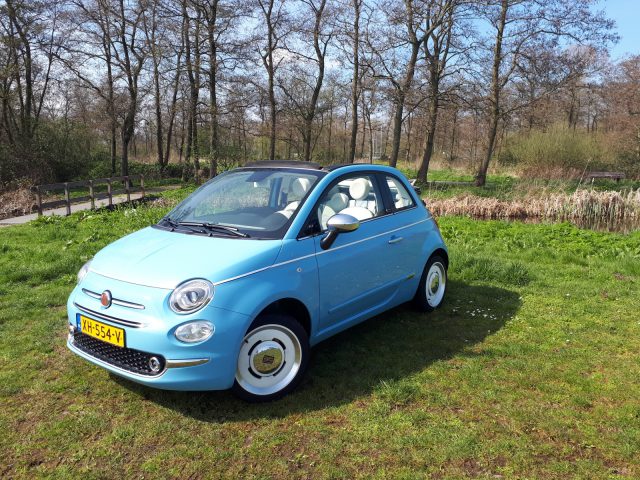 In het gras staat een blauwe Fiat 500C Spiaggina '58 geparkeerd.
