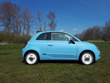 Een blauwe Fiat 500C Spiaggina '58 staat geparkeerd in een grasveld.