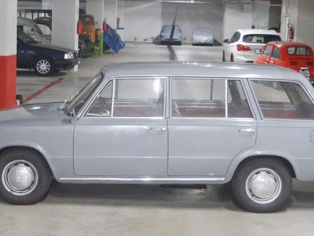 Een oude grijze auto staat geparkeerd in een garage 124.