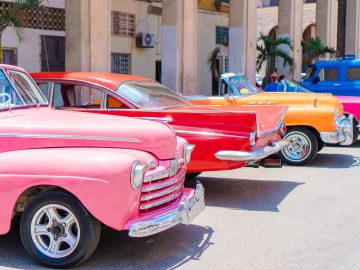 Een rij oldtimers in verschillende kleuren geparkeerd voor een gebouw.