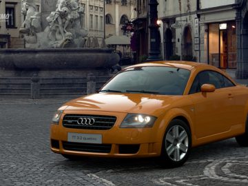 Een oranje Audi Gran Turismo-auto staat geparkeerd op een geplaveide straat.