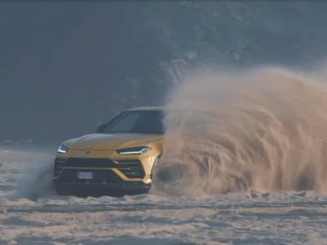 Een gele Urus die door zand op een strand rijdt.