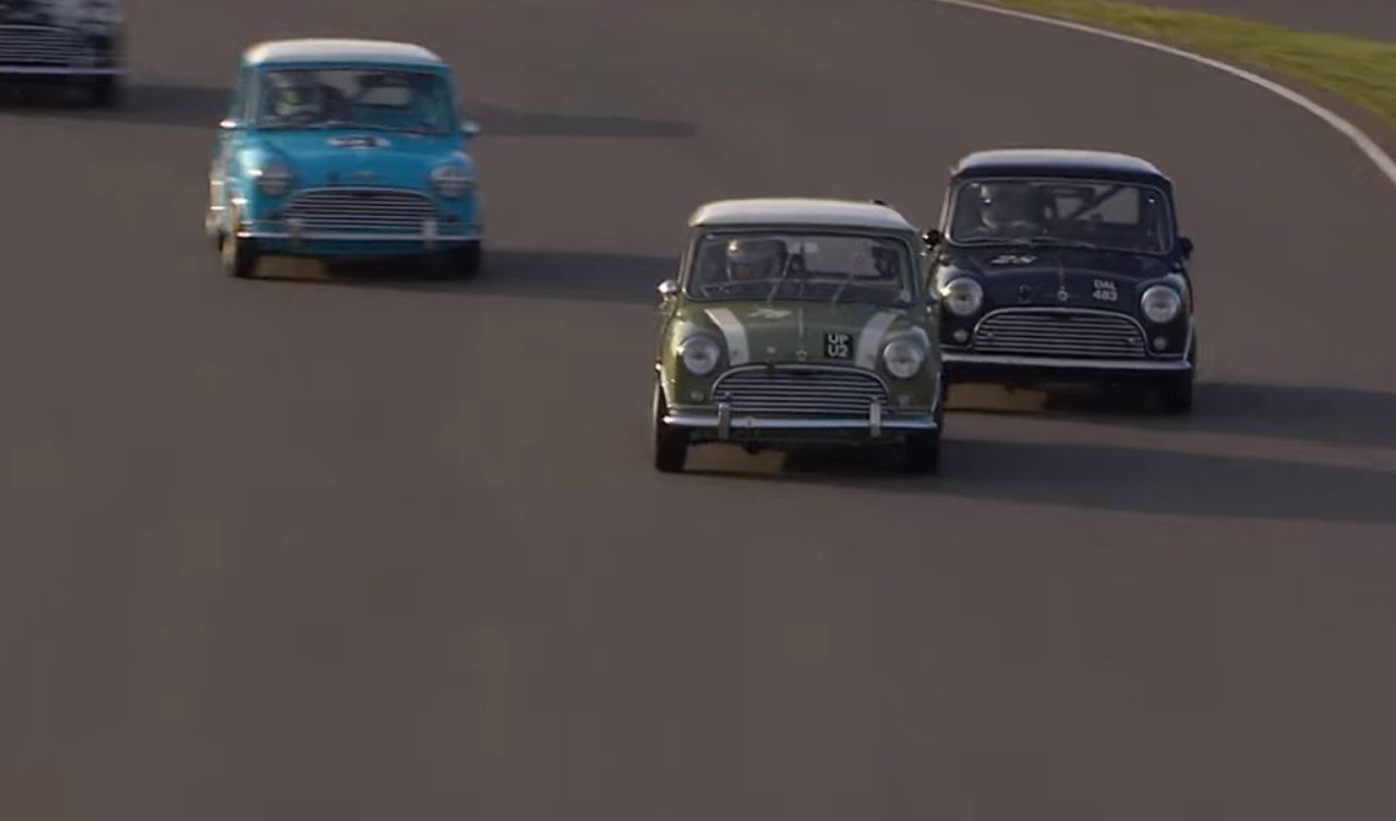 Een groep klassieke miniauto's die over een racecircuit rijden.