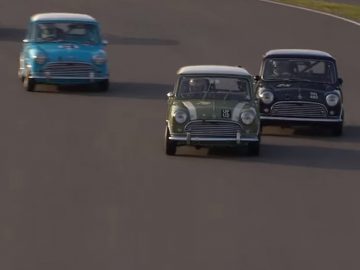 Een groep klassieke miniauto's die over een racecircuit rijden.